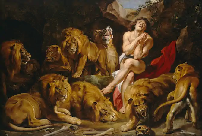 A dramatic Baroque painting depicting Daniel in the lions' den. A muscular male figure in minimal white cloth sits praying amid several large lions in a dark cave. The lions, painted in rich golden tones, surround him menacingly, with some showing their teeth. Human bones and skulls lie scattered on the ground. A patch of blue sky is visible through an opening in the cave ceiling.