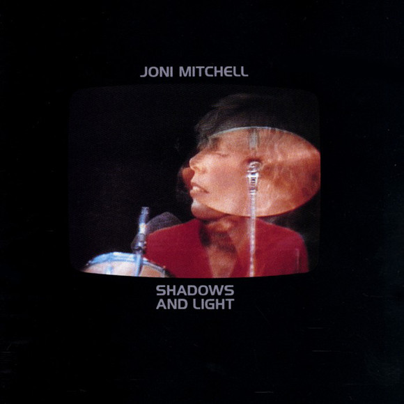 Album cover of Shadows and Light. Black with a semi-transparent view of Mitchell's face superimposed over a cymbal.