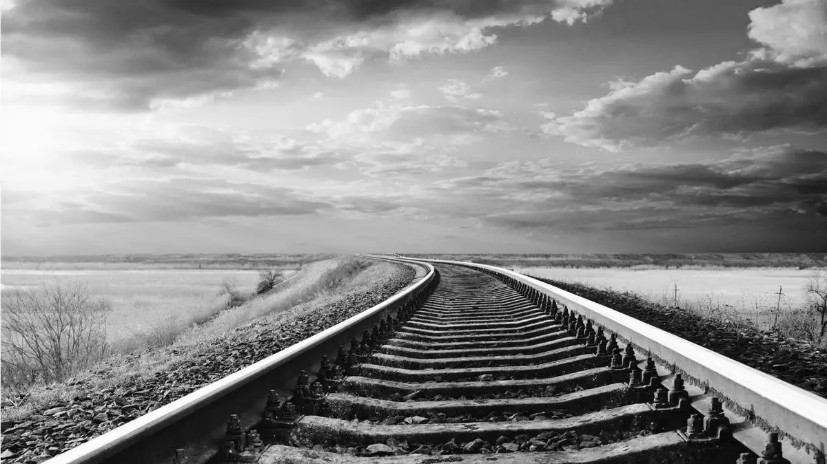 A black and white photo viewed as one standing between train rails watching them curve away into the distance.