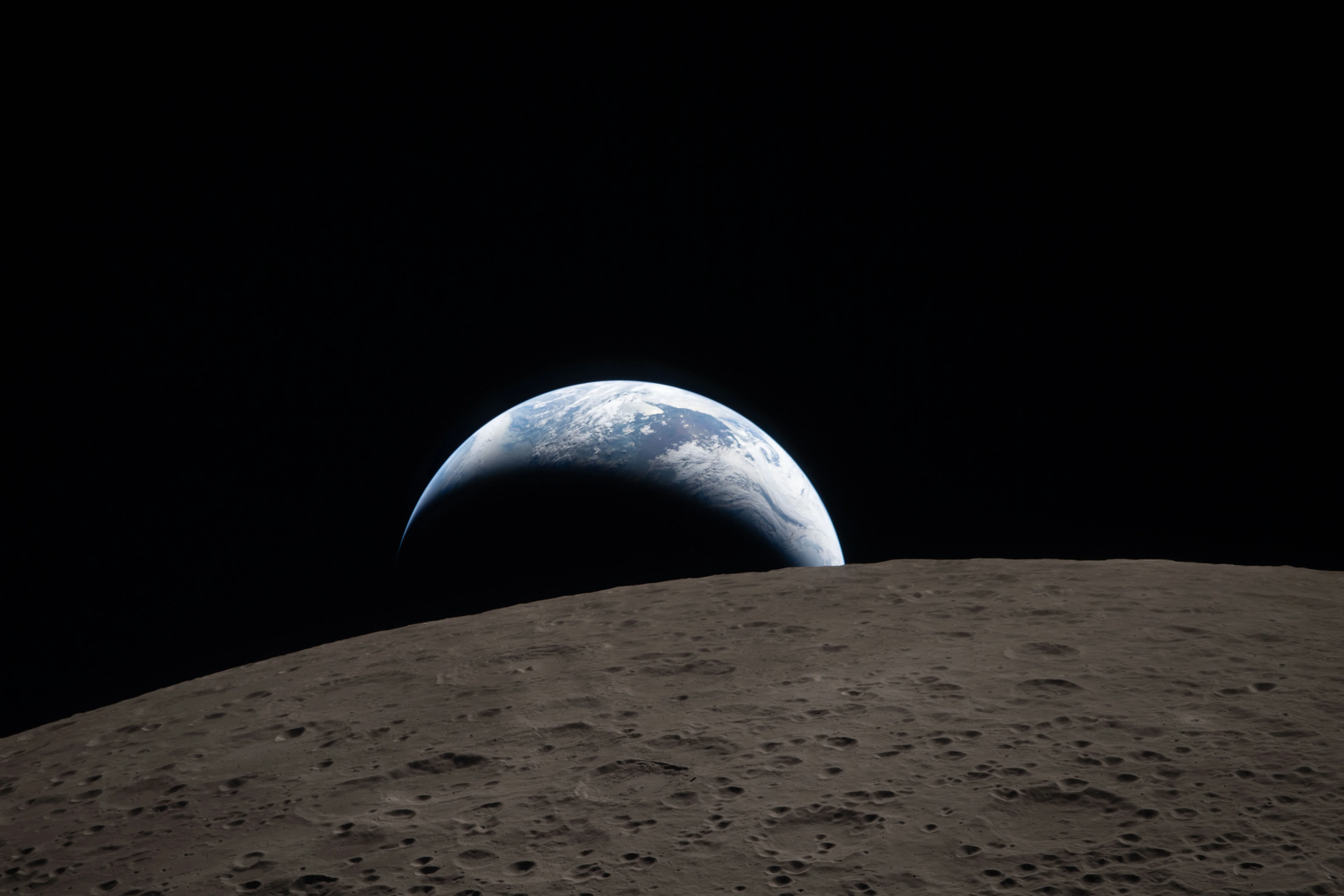 (April 6, 2026) – Earthset captured through the Orion spacecraft window at 6:41 p.m. EDT, April 6, 2026, during the Artemis II crew’s flyby of the Moon. A muted blue Earth with bright white clouds sets behind the cratered lunar surface. The dark portion of Earth is experiencing nighttime. On Earth’s day side, swirling clouds are visible over the Australia and Oceania region. In the foreground, Ohm crater has terraced edges and a flat floor interrupted by central peaks—formed when the surface rebounded upward during the impact that created the crater.