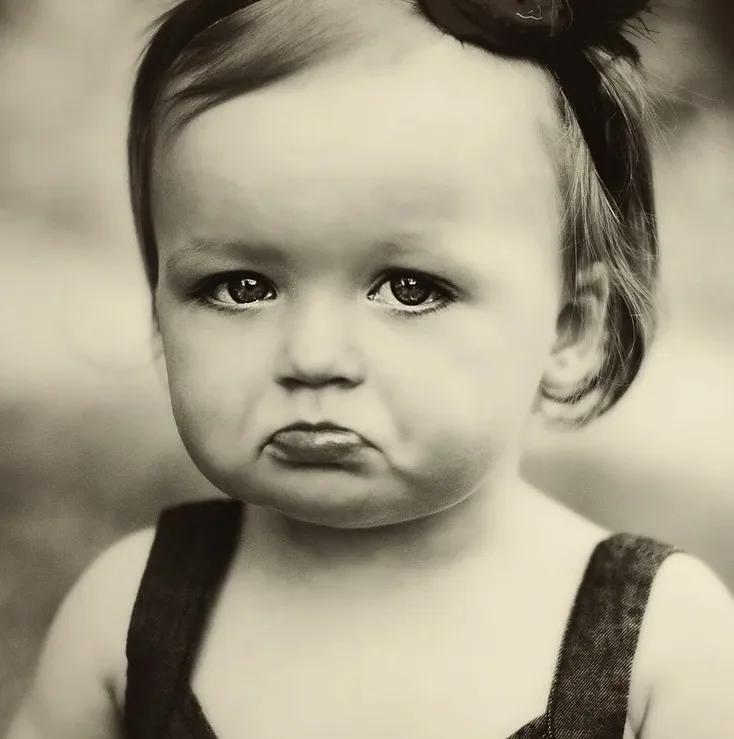 Black and white photo of a child with a big grumpy frown.
