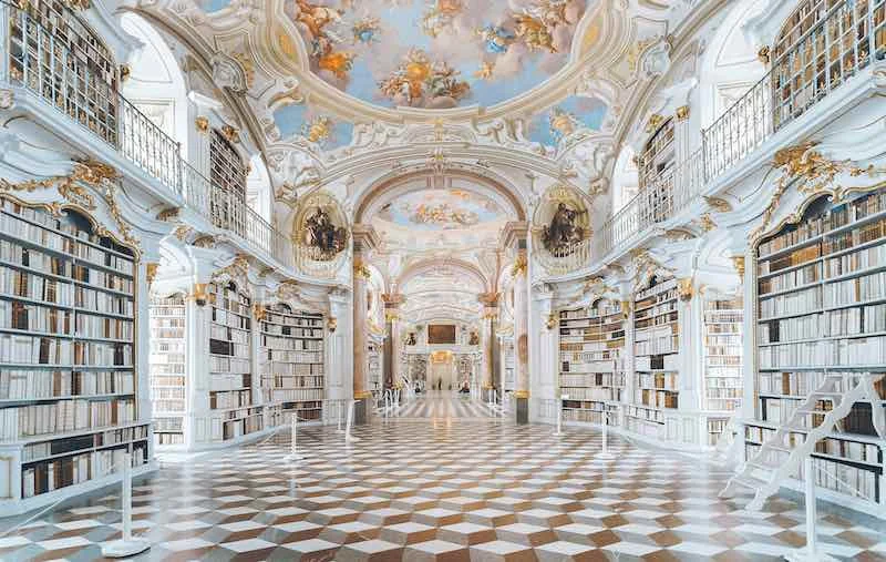 Brightly lit palatial library. Location unknown."