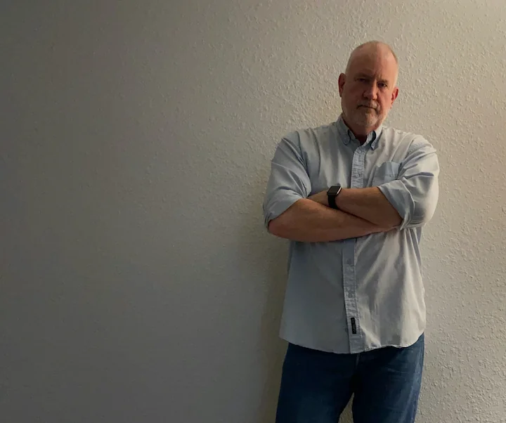 Me, standing against a wall. Arms folded across. Blue button down. Jeans.