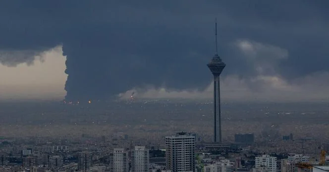 A cityscape of Tehran with the Milad Tower standing tall amidst dense, dark clouds and a plume of smoke in the distance, creating a dramatic and ominous atmosphere.