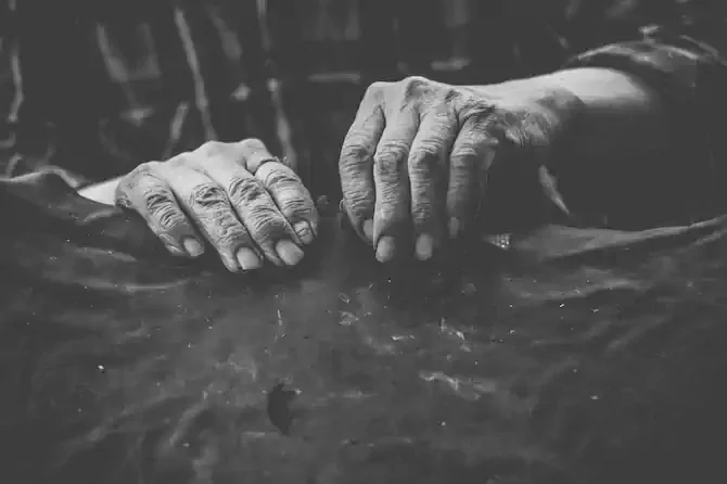 Black and white photo of aged hands working on a sheet of fabric.