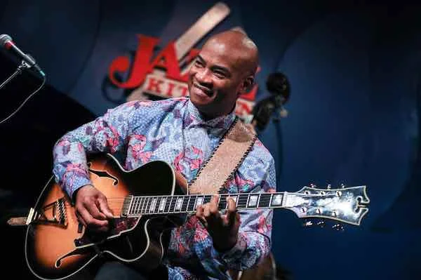 Russell Malone seated, playing his guitar.