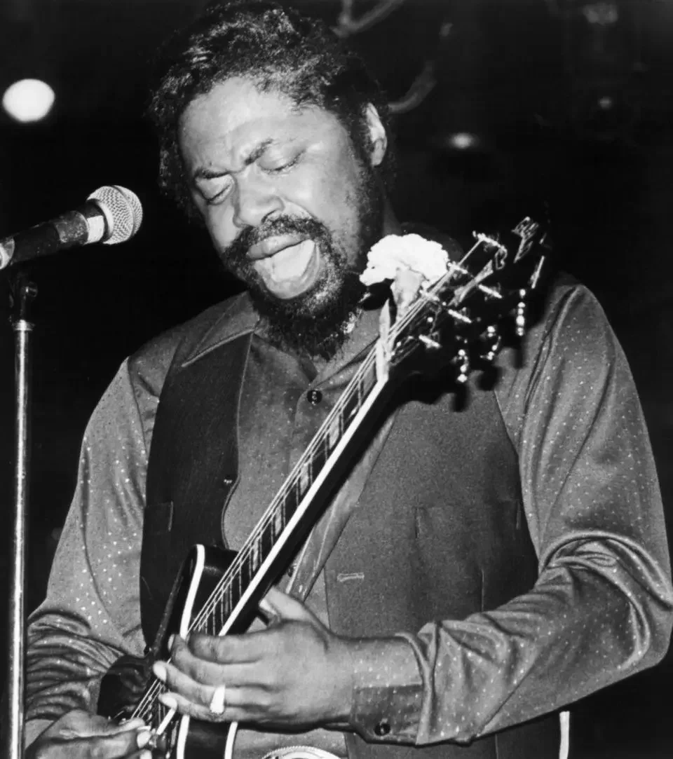 Black and white photo of bluesman Son Seals playing his guitar on stage.
