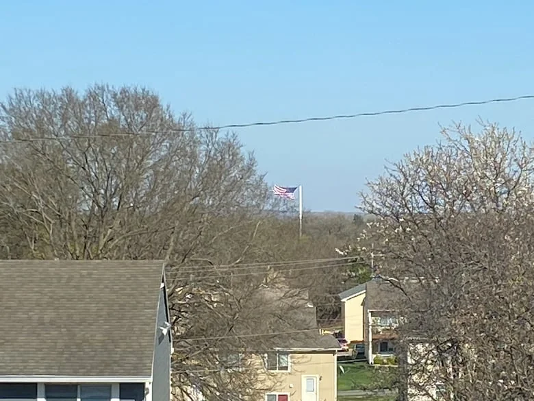 Photo shows a flagpole in the distance with a U.S. flag standing straight out from a strong wind.